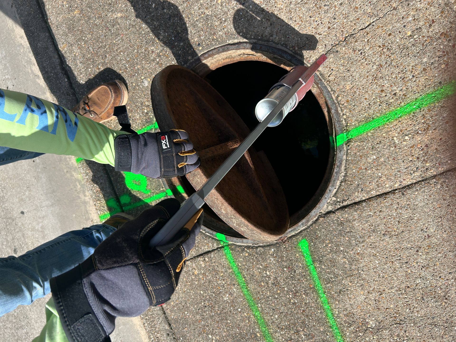 Technician opening a manhole with green utility markings painted around it